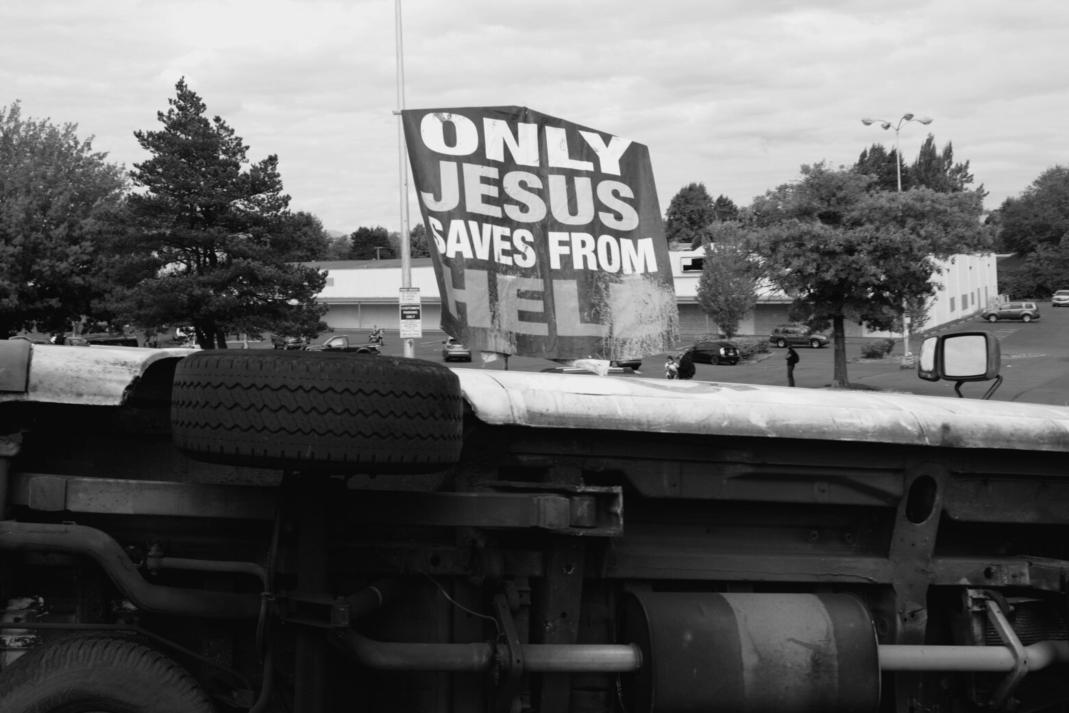 A photograph of an overturned van in a parking lot. In the background, a sign reads: 'Only Jesus saves from hell' in all caps.